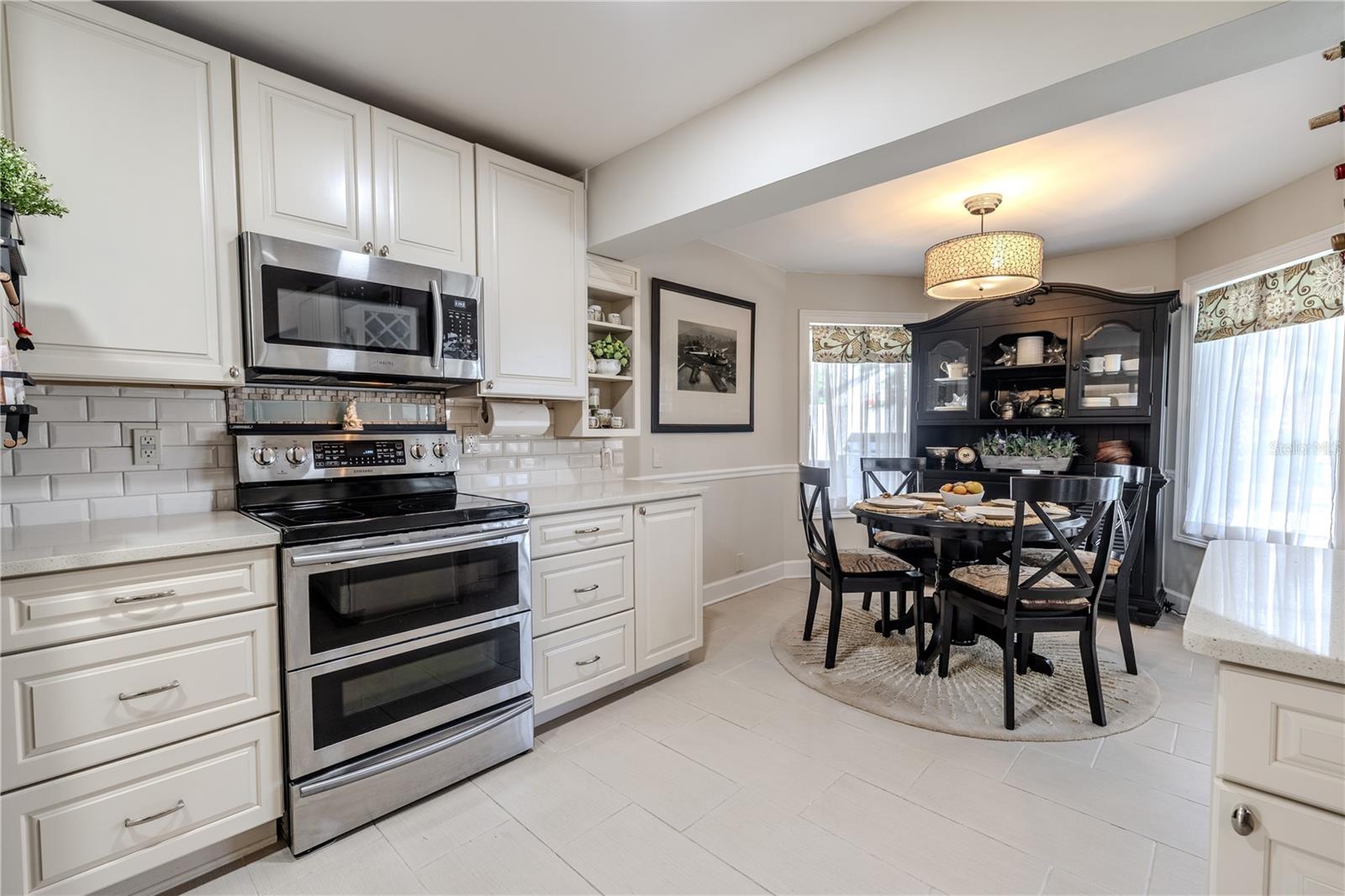 Custom-designed white cabinetry with beveled subway tiled walls, chair rails and built-in display shelving frames the kitchen and dining nook, blending tailored storage with an elegant, timeless presentation.