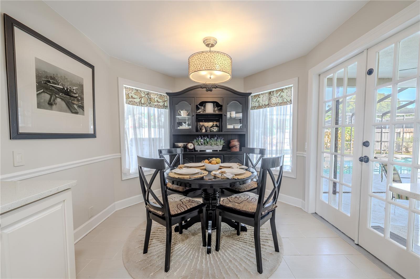 Custom window treatments with patterned valances and sheer panels frame the dining nook, softly filtering natural light while adding a refined, tailored finish to the space with french door access to the lanai.