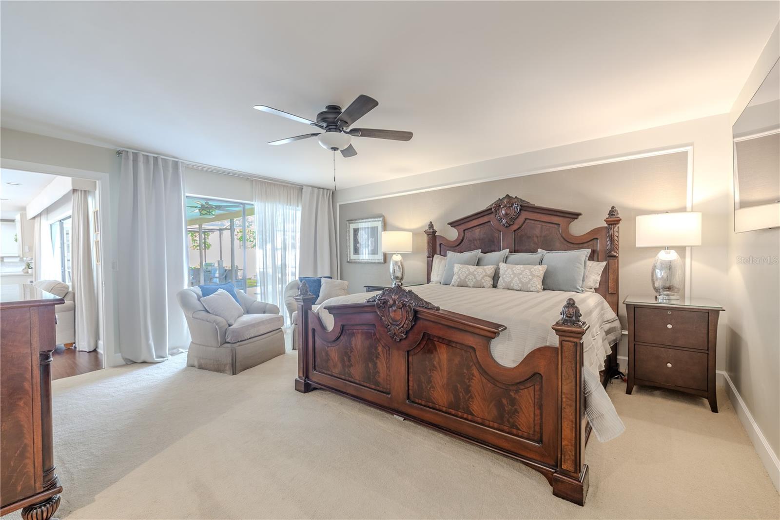 The spacious primary suite features plush carpeting, a ceiling fan, and direct sliding-glass-door access to the screened lanai, complemented by a generous en-suite bathroom offering abundant space and a serene, spa-like retreat.