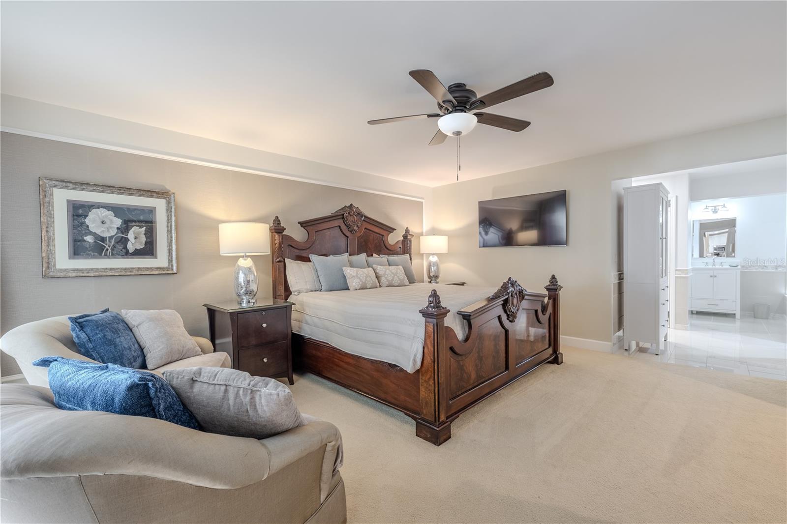 The spacious primary suite features plush carpeting, a ceiling fan, and direct sliding-glass-door access to the screened lanai, complemented by a generous en-suite bathroom offering abundant space and a serene, spa-like retreat.