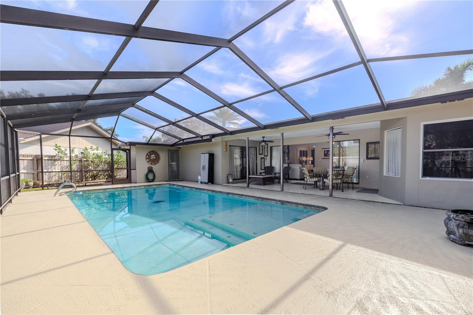 A bright, screened-in pool and patio area featuring a newly birdcage enclosure (top rescreened in 2025, deck repainted 2025), creating a clean, open-air feel with protected views of the pool and covered outdoor living space.