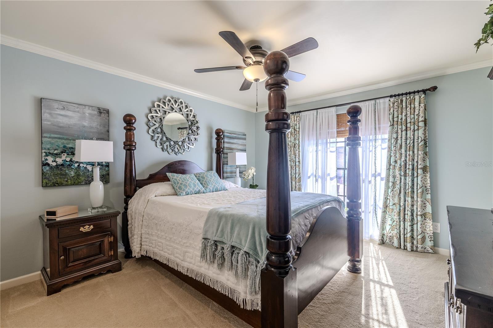 This third bedroom offers a warm, inviting retreat featuring plush carpeting, a ceiling fan, elegant crown molding, and abundant natural light through floor-length windows with custom window treatments, making it ideal for guests or a comfortable secondary bedroom.