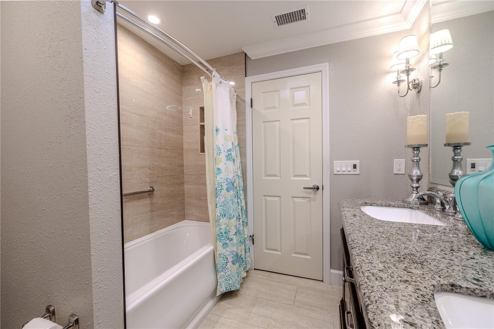 The second bathroom features a tub/shower combination with neutral large format tile surround, granite countertop vanity, crown molding, and updated lighting for a clean, polished finish.