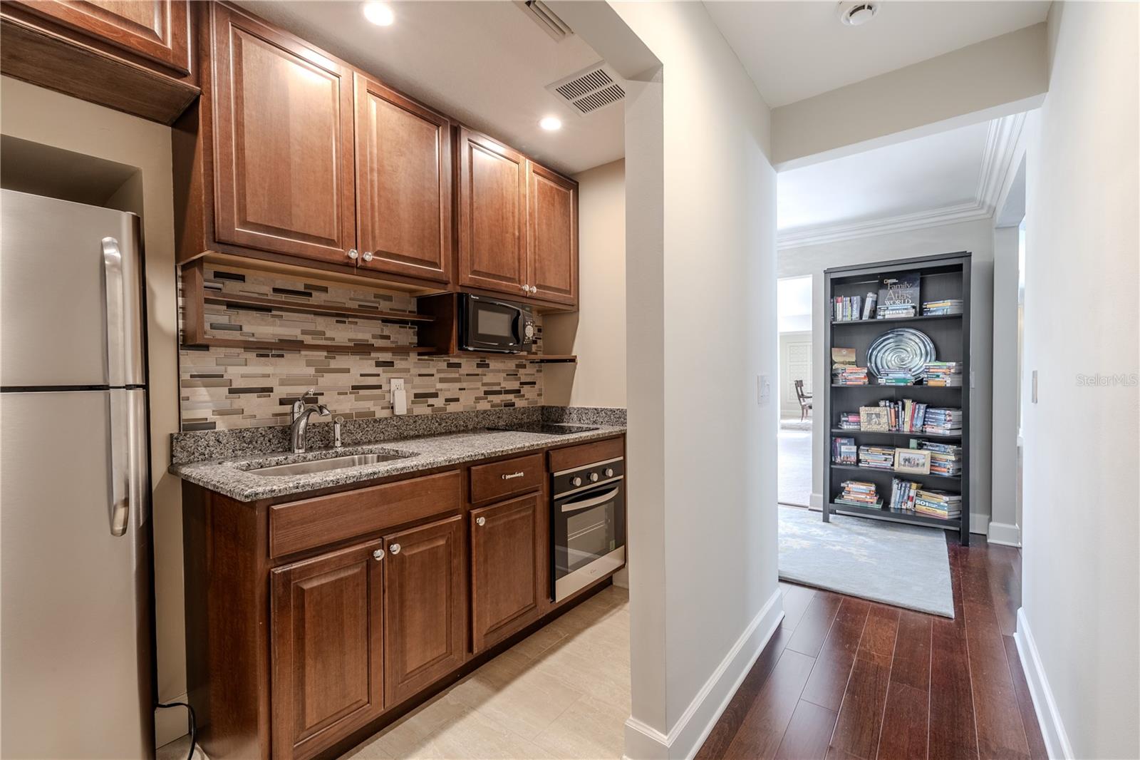 This well-appointed secondary kitchen nook offers granite countertops, custom wood cabinetry, mosaic tile backsplash, stainless appliances, and recessed lighting, seamlessly positioned just off the main living areas for flexible everyday or guest use.