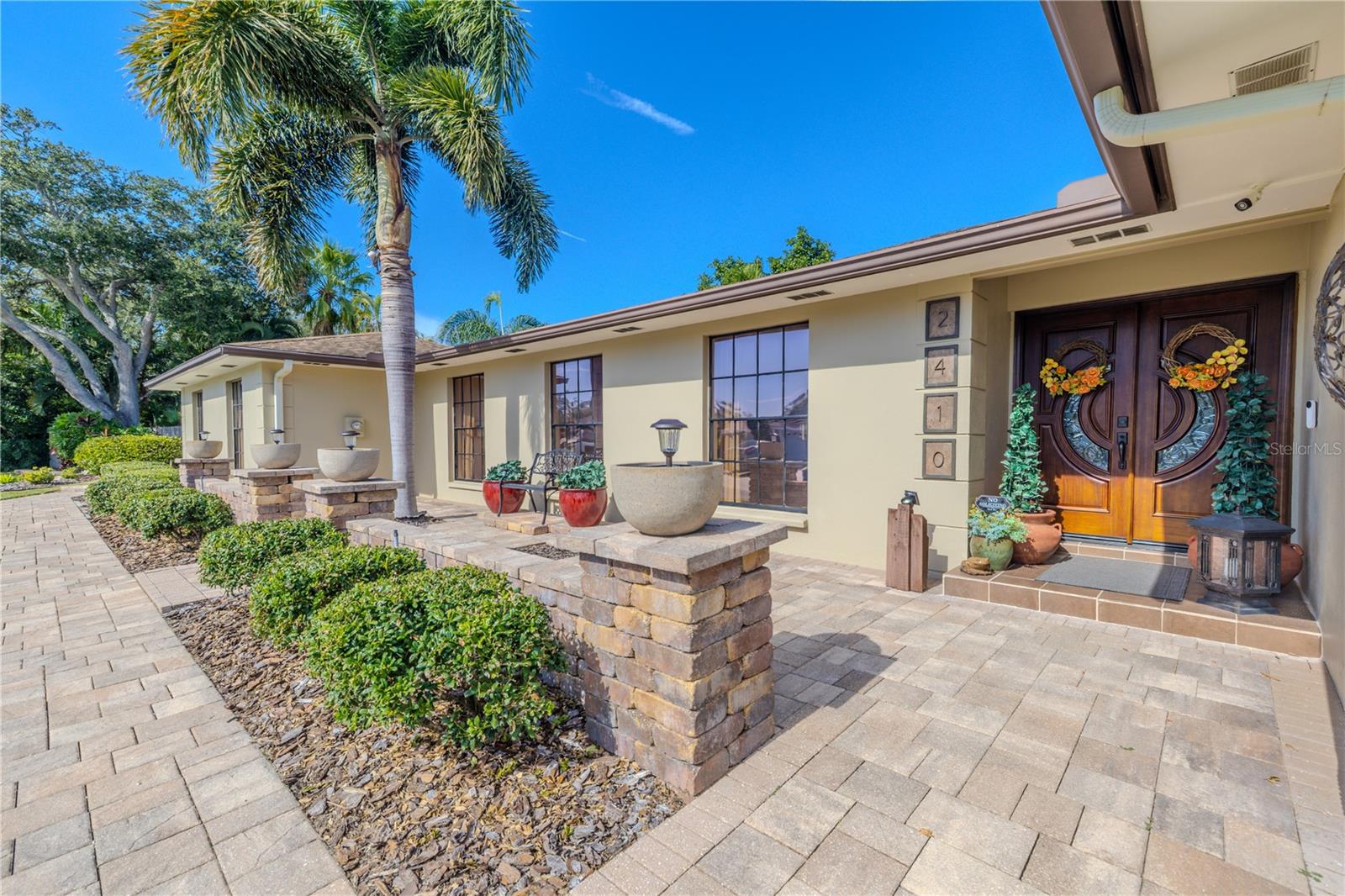 Striking, custom solid-wood double entry doors imported from Malaysia anchor the front façade, creating a warm, upscale first impression complemented by stone accents, manicured landscaping, and a paver walkway.