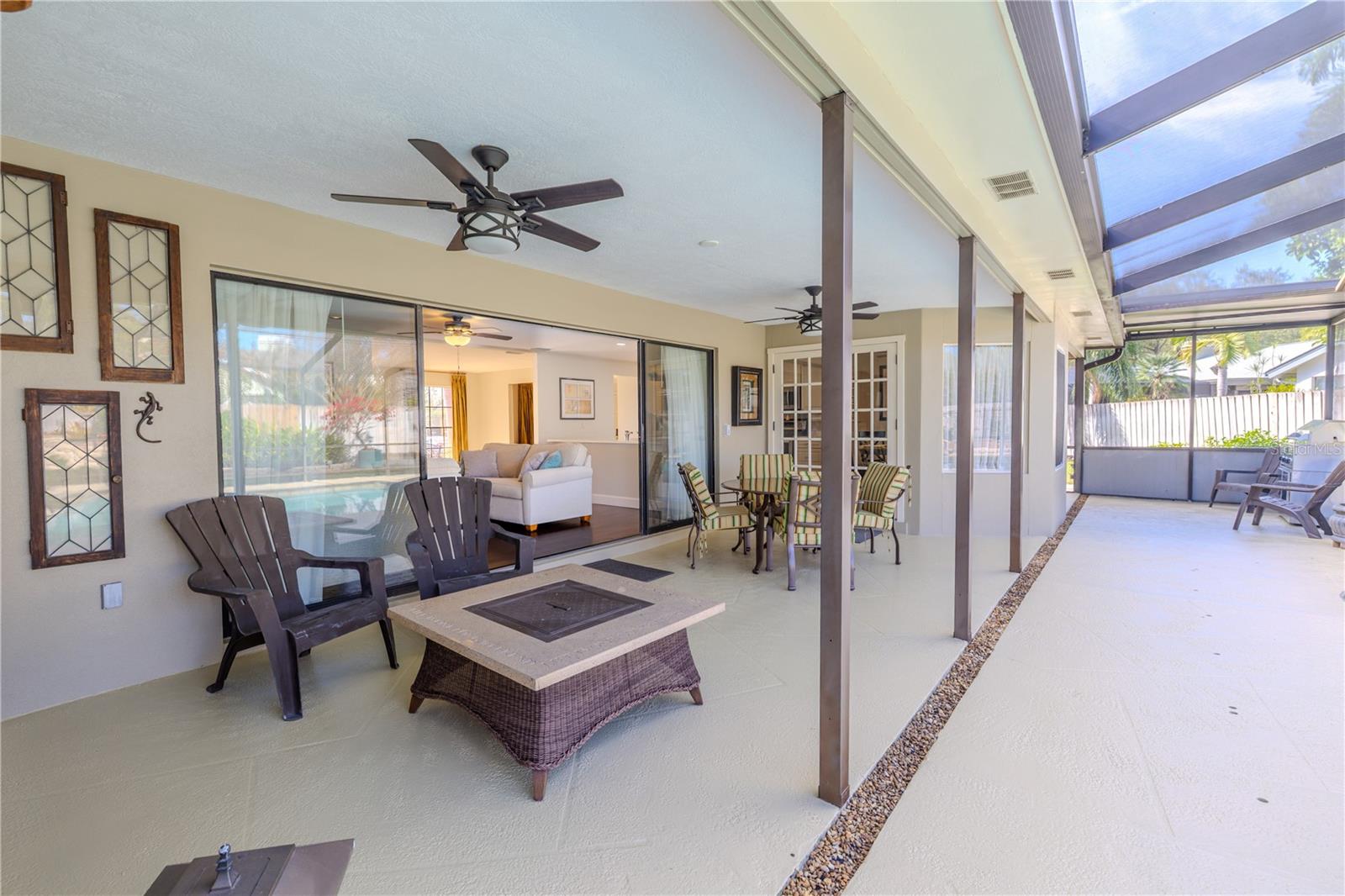 This expansive screened lanai offers a true indoor–outdoor living experience, featuring multiple ceiling fans, generous seating areas, a fire table, and wide sliding glass doors that seamlessly connect to the family room while overlooking the screened private pool area.