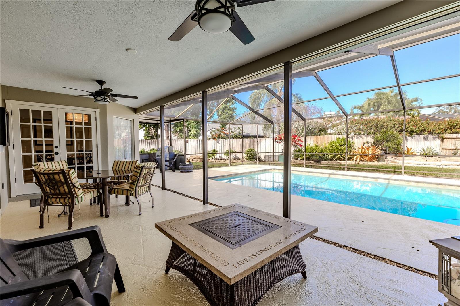 This spacious screened-in lanai overlooks the sparkling pool and features multiple ceiling fans, a dining area, and a cozy fire table—creating an ideal setting for year-round outdoor entertaining and relaxation.