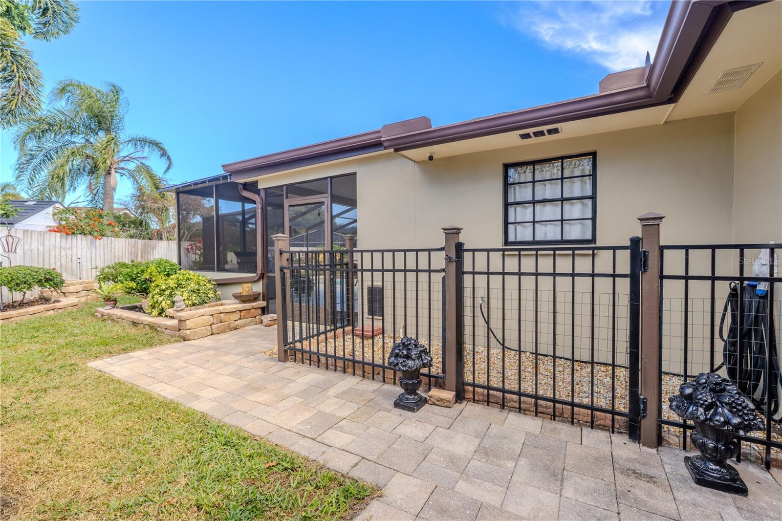 The fenced side yard doggy area with doggy door laundry room access features a paver walkway with gated access, neatly landscaped beds, and direct connection to the screened lanai, offering a secure and low-maintenance outdoor space ideal for pets or gardening.