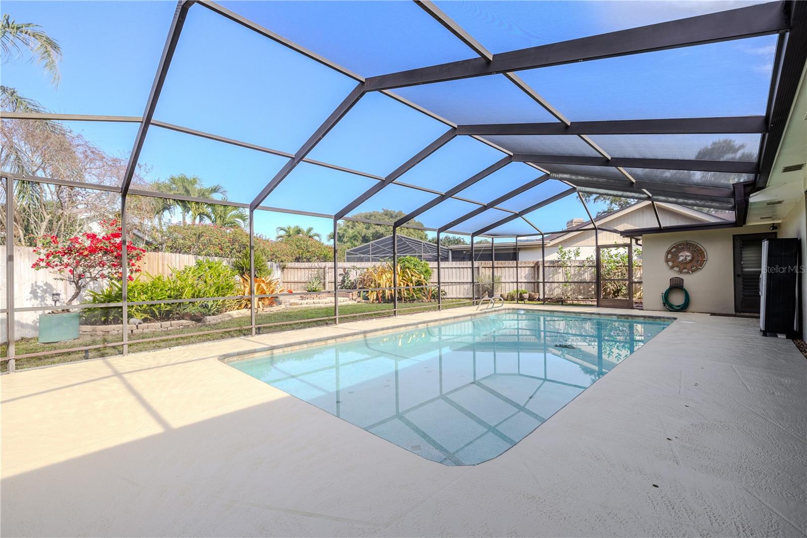 The screened-in pool enclosure (top re-screened in 202) showcases a spacious repainted deck (2025), crystal-clear swimming pool (pool resurfaced in 2014, pump rebuilt in 2024), and lush tropical landscaping beyond the enclosure, creating a private, resort-style outdoor retreat ideal for year-round enjoyment.
