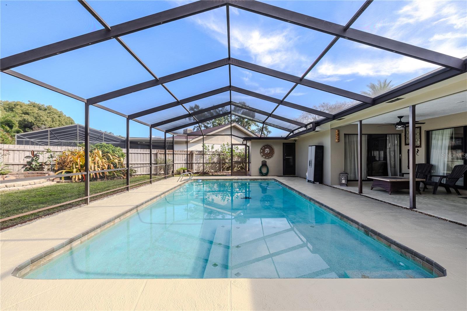 The screened-in swimming pool features clear sight lines under a freshly re-screened enclosure top, a recently repainted deck (2025), storage shed, and an adjoining covered lanai, creating a private, low-maintenance outdoor living space ideal for relaxing or entertaining year-round.