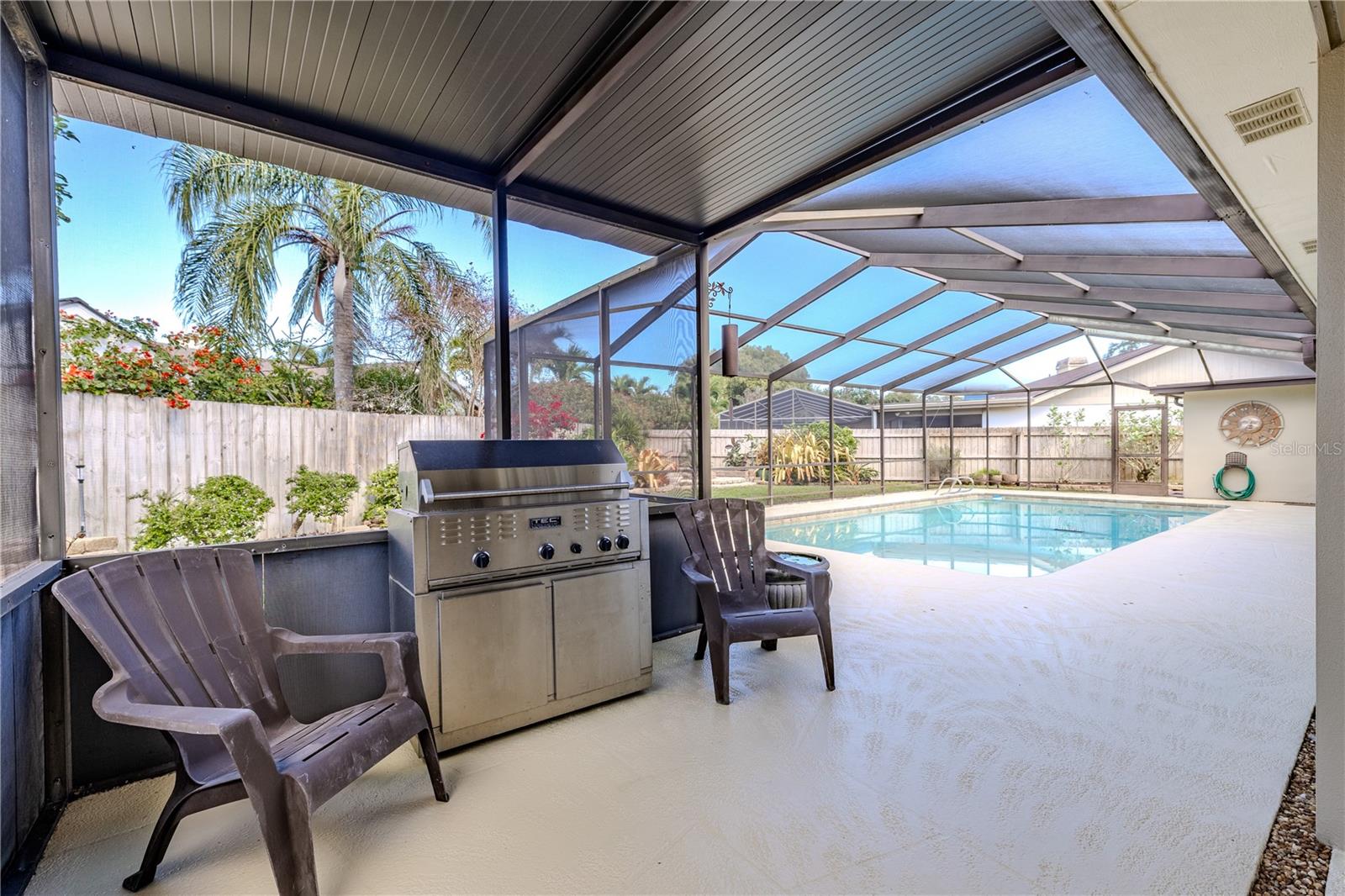 The covered outdoor grilling area overlooks the screened-in pool and freshly painted deck, offering a shaded, functional space ideal for year-round entertaining and relaxed outdoor living.