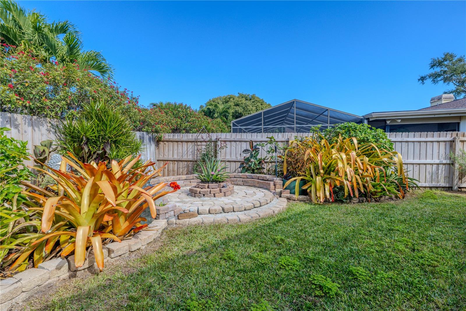 A thoughtfully landscaped backyard retreat featuring a circular stone garden centerpiece, lush tropical plantings, and privacy fencing—creating a serene, park-like setting that complements the home’s outdoor living spaces.