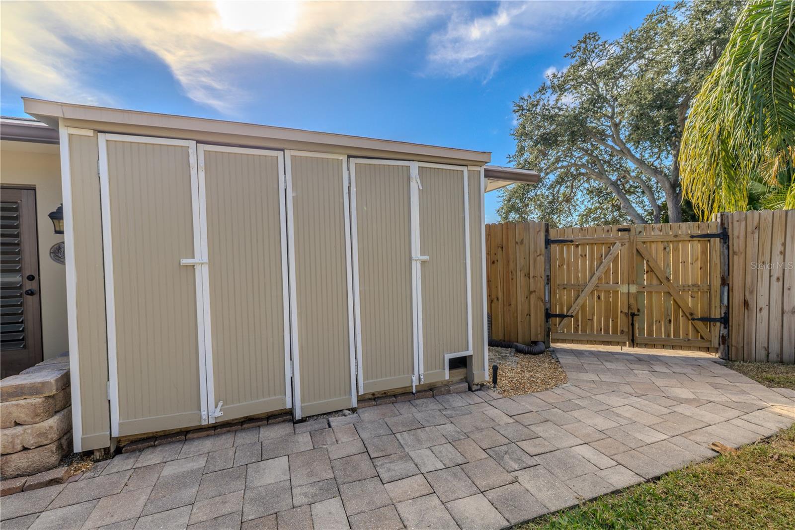 A clean, well-maintained dual storage shed setup lines the paved side yard, paired with a wide gated access—ideal for secure storage, yard equipment, and easy in-and-out functionality.