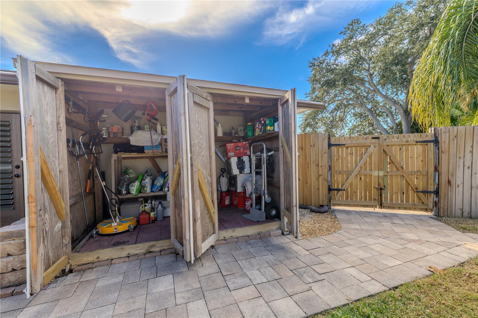 Dual outdoor storage sheds provide ample space for tools, equipment, and seasonal items, conveniently set along the paved side yard with gated access for easy organization and functionality.