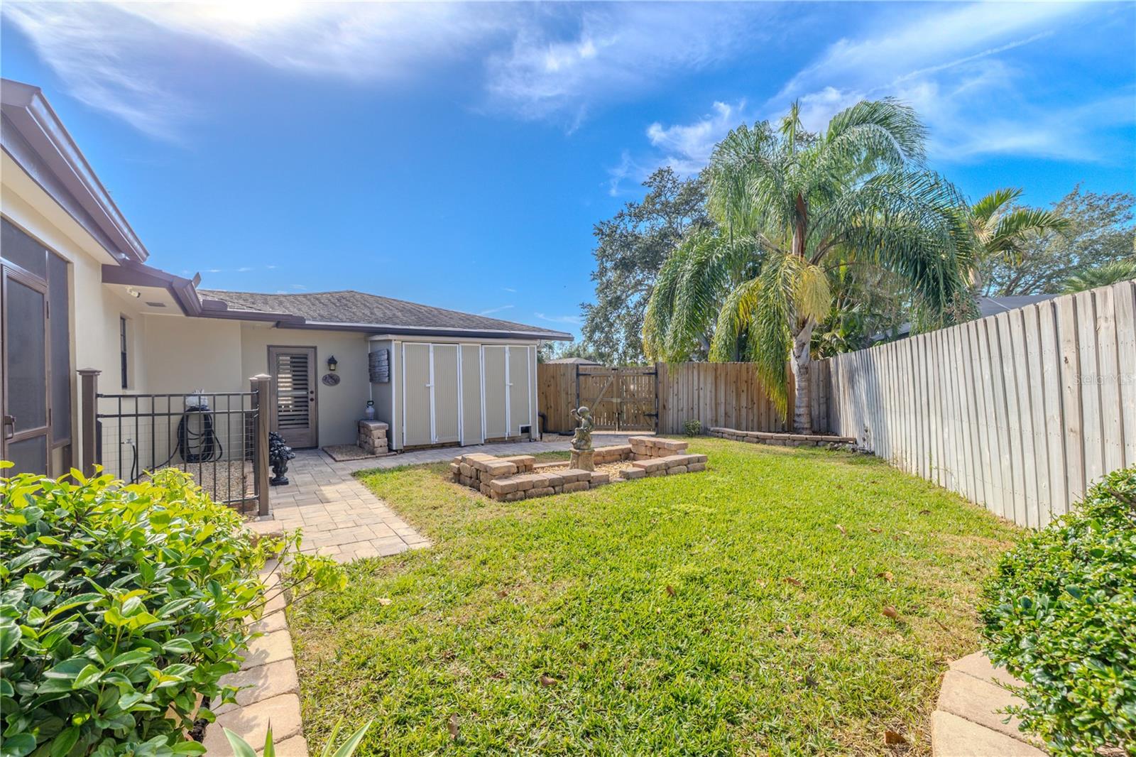 A wider view of the fully fenced backyard includes dual storage sheds for added convenience, along with a paver walkway, dual gated access, and a grassy yard ideal for storage, hobbies, or outdoor enjoyment.
