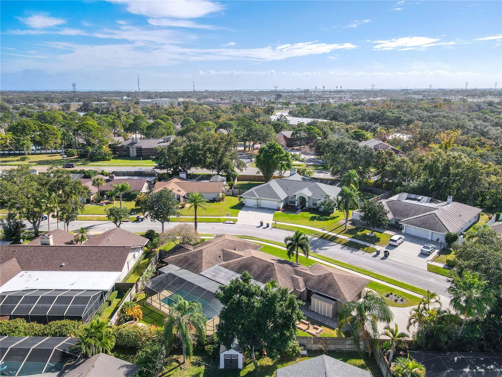 A panoramic south-facing aerial view highlights the home’s position within a quiet, well-established neighborhood, framed by mature trees, manicured lawns, and long sight lines toward the surrounding residential and commercial landscape under open Florida skies.