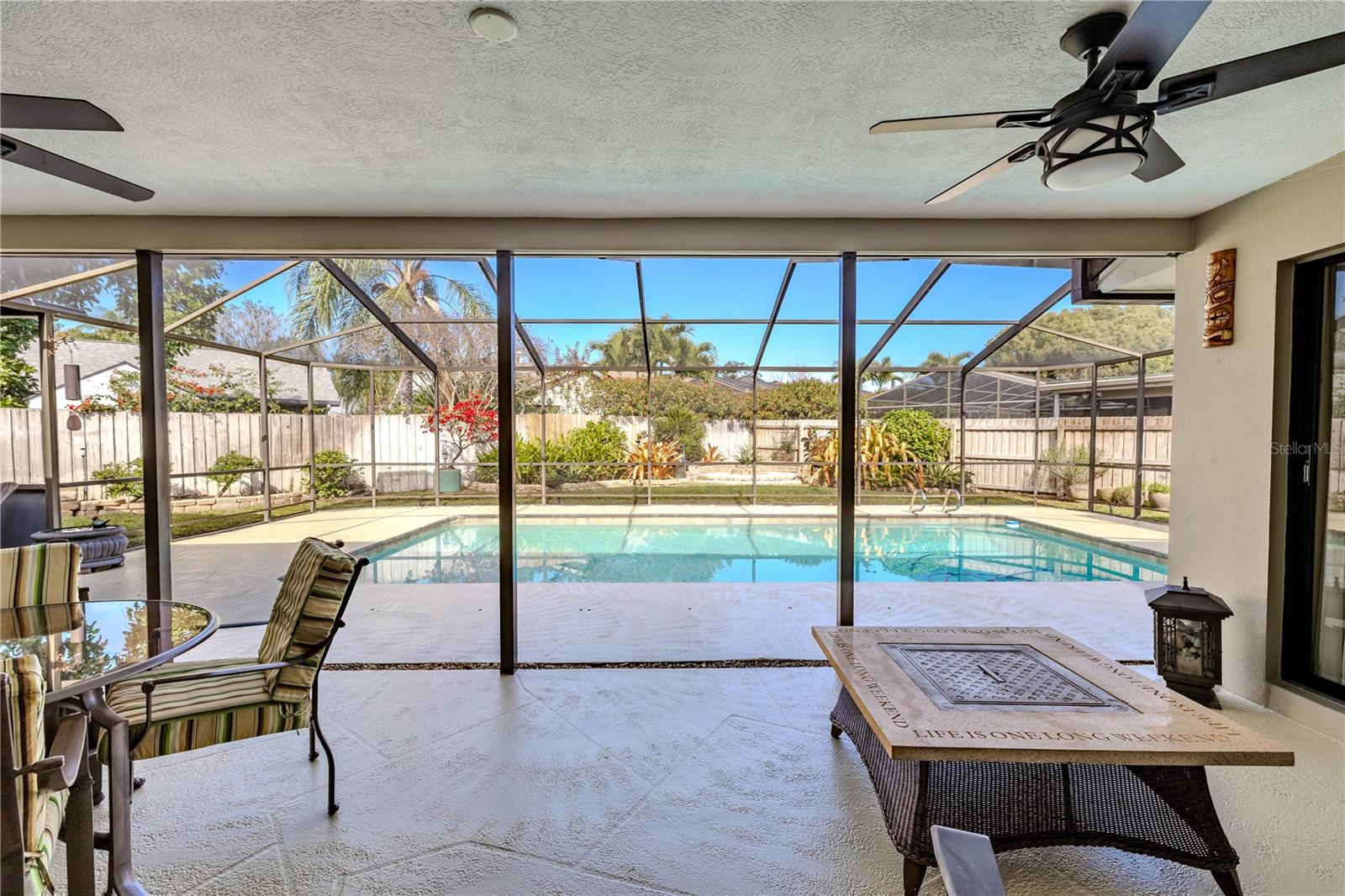 View from the family room through expansive sliding glass doors to the screened lanai, showcasing the private pool, spacious covered patio, ceiling fans, and a tranquil, fully fenced backyard oasis ideal for seamless indoor-outdoor living.