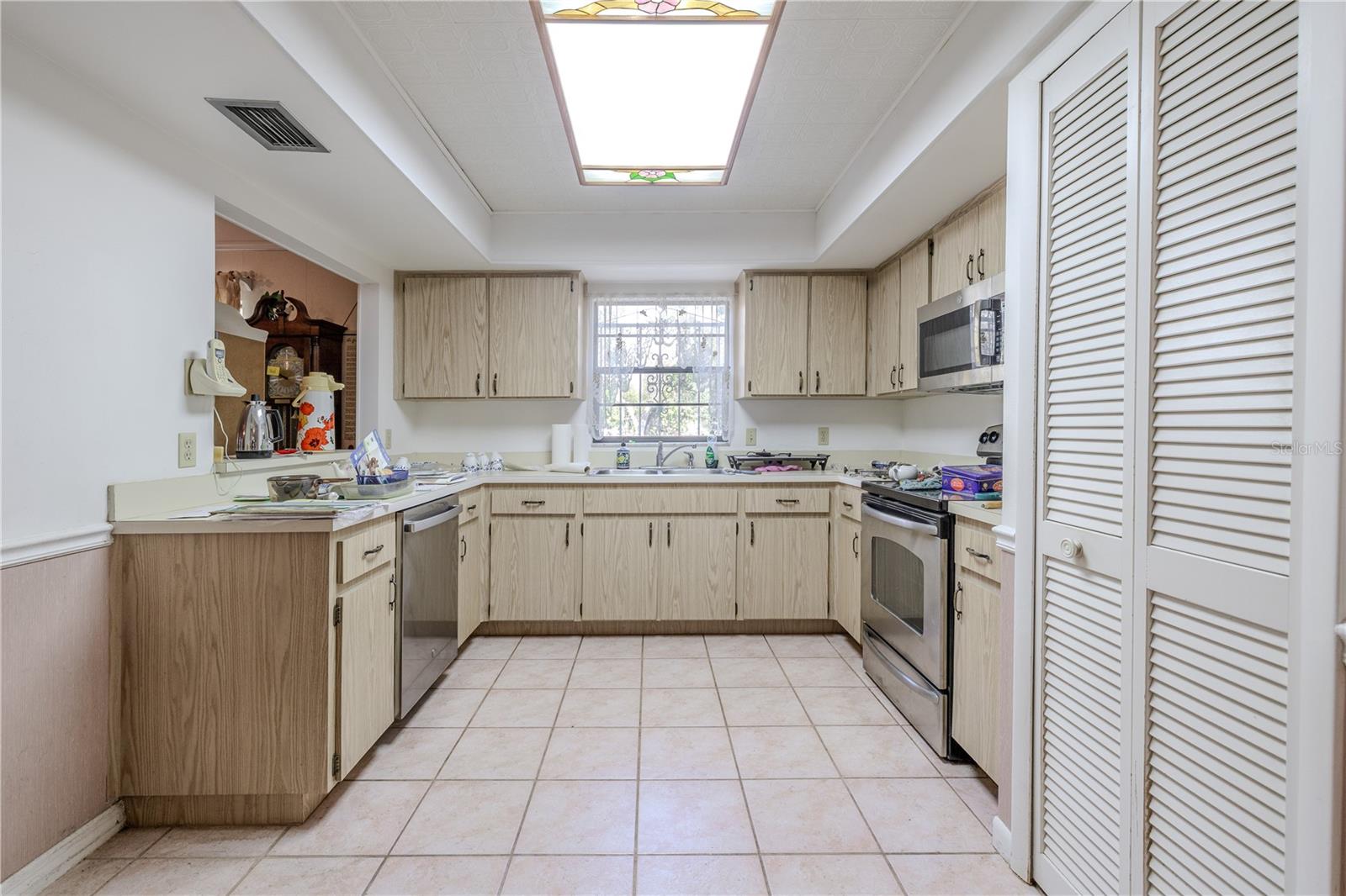 Bright, functional 20.5 X 10.9 kitchen with a passthrough counter, tile flooring, abundant cabinetry and counter space, large pantry, and stainless appliances including a built-in microwave and range.