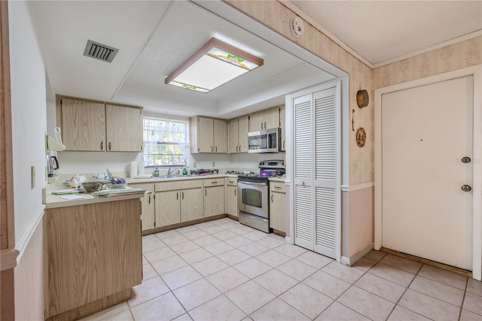 Additional view of the functional kitchen with tile flooring, abundant cabinetry and counter space, large pantry, and stainless appliances including a built-in microwave and range with garage entry.
