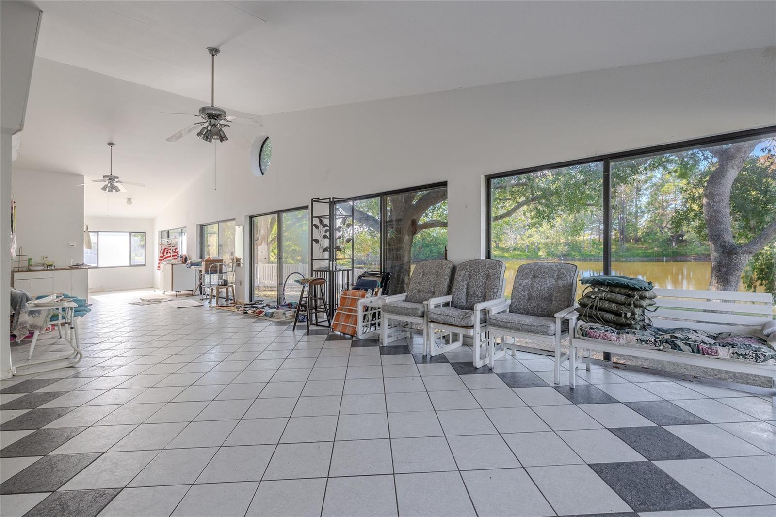 Another view of the air-conditioned fully enclosed Florida room with tile flooring, ceiling fans, and a wall of windows and sliding glass doors overlooking the yard and pond.