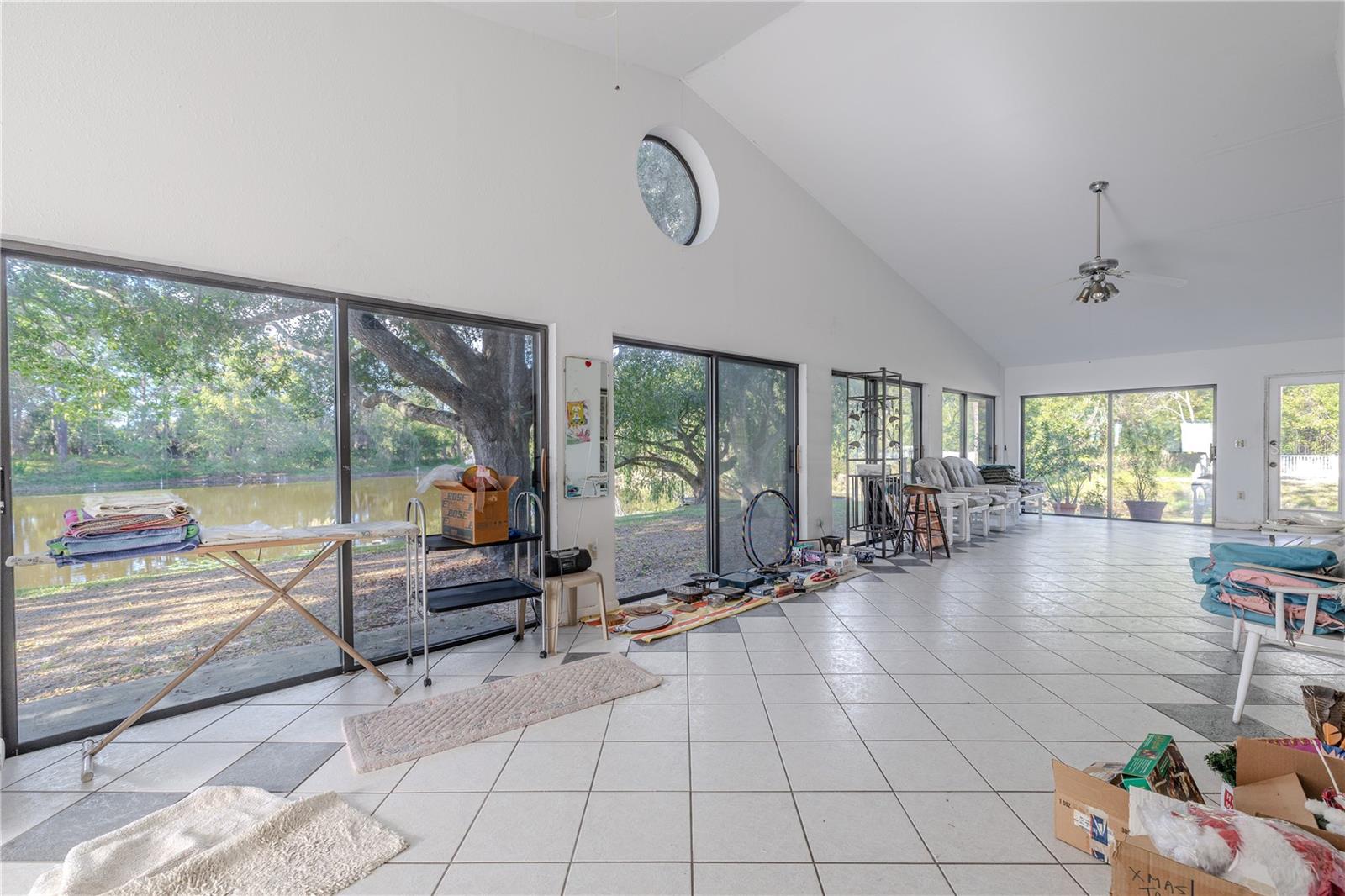 Another view of the fully air-conditioned enclosed 52 X 14 ft. Florida room with tile flooring, vaulted ceiling, ceiling fans, port hole upper window, and a wall of windows and private entry door overlooking the yard and pond.