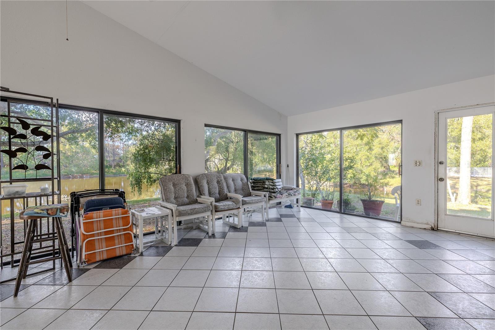 Corner view of the Florida room with tile flooring, vaulted ceiling, and a wall of windows that open to the expansive backyardand pond.