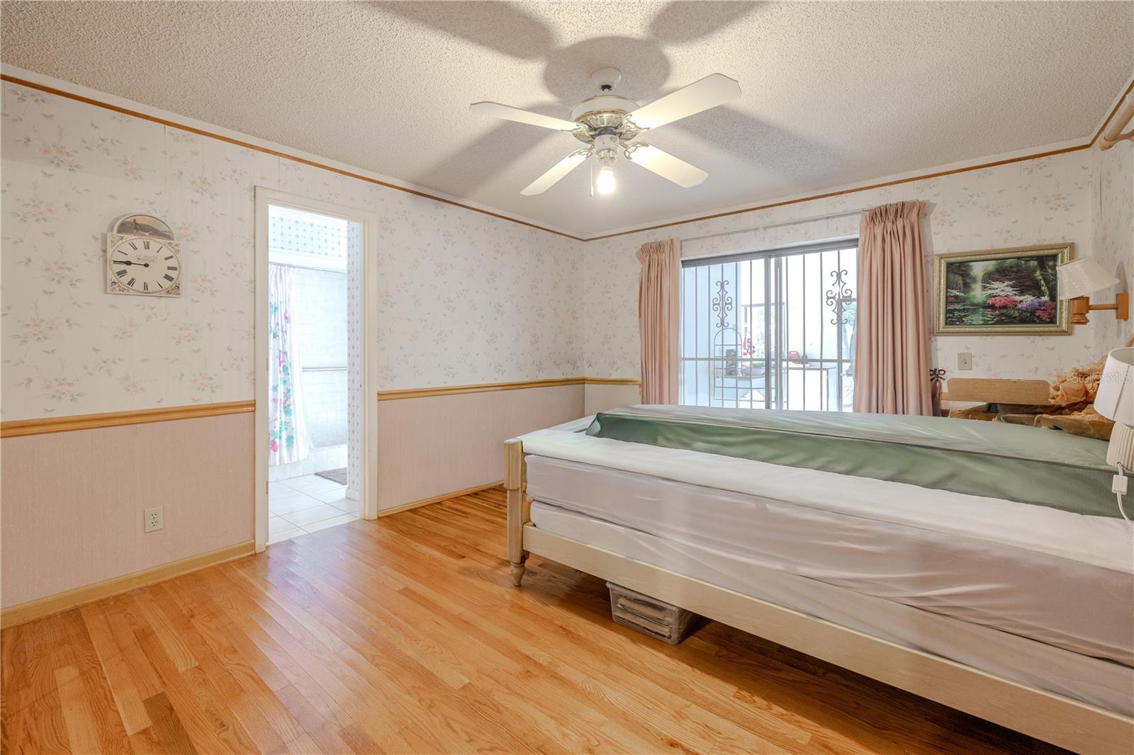 Spacious primary 15.6 X 12.1 bedroom with hardwood floors, ceiling fan, ample natural light, and a private en-suite bath.