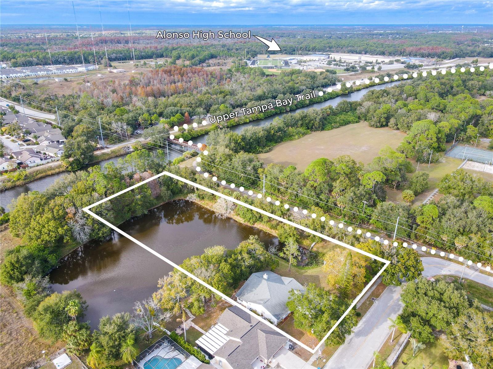 Aerial view highlights the home’s private, tree-lined lot with direct pond frontage—approximately one-third of the pond is included with the property—nestled in an established neighborhood with a serene natural backdrop.