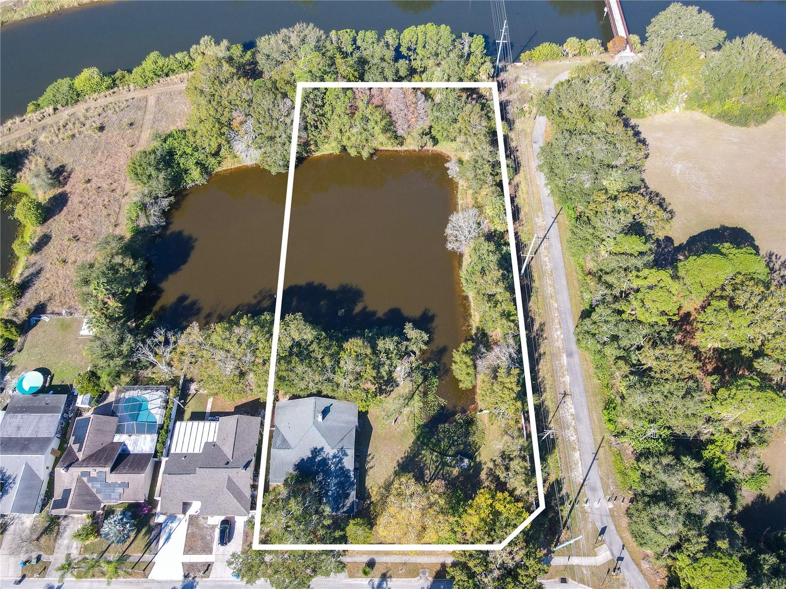 Front aerial overview showing the property boundary with its expansive pond, lush tree canopy, and prime Bay Port Colony location near Tampa Bay, wetlands, Upper Tampa Bay Trail, and major routes.