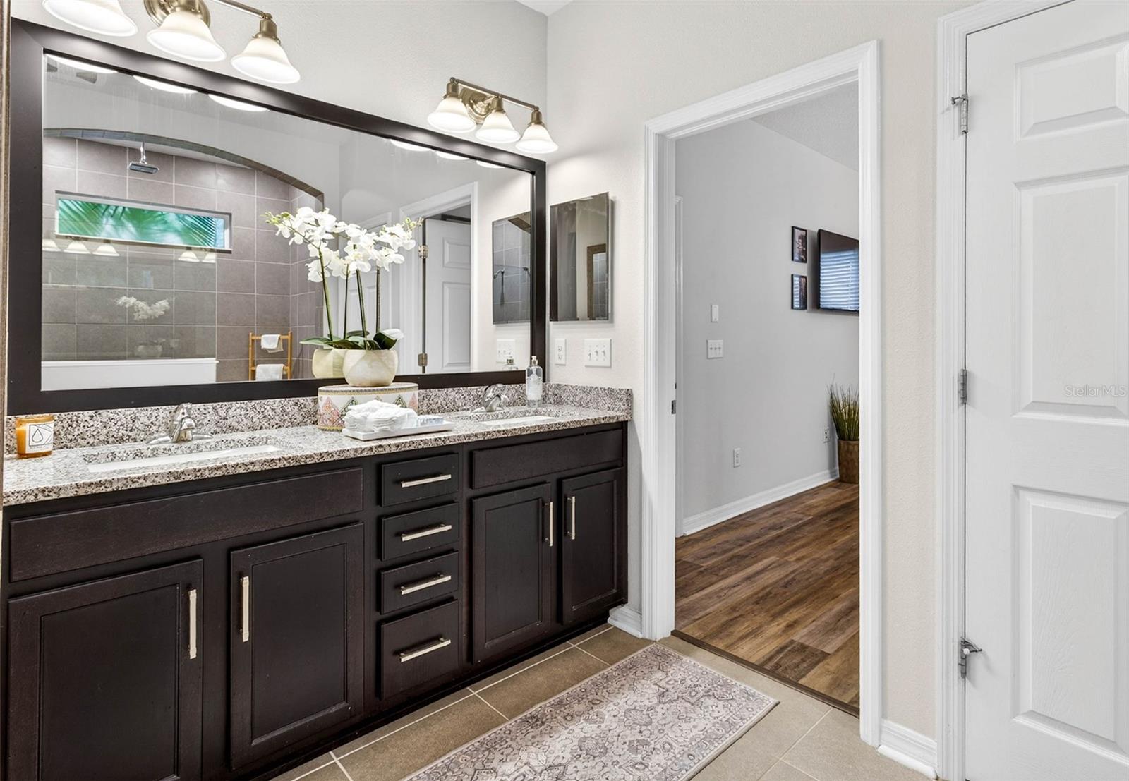 Comfort height vanity with dual sinks and tiled flooring is located off of the primary bedroom. Door to wash closet is also pictured on the right.