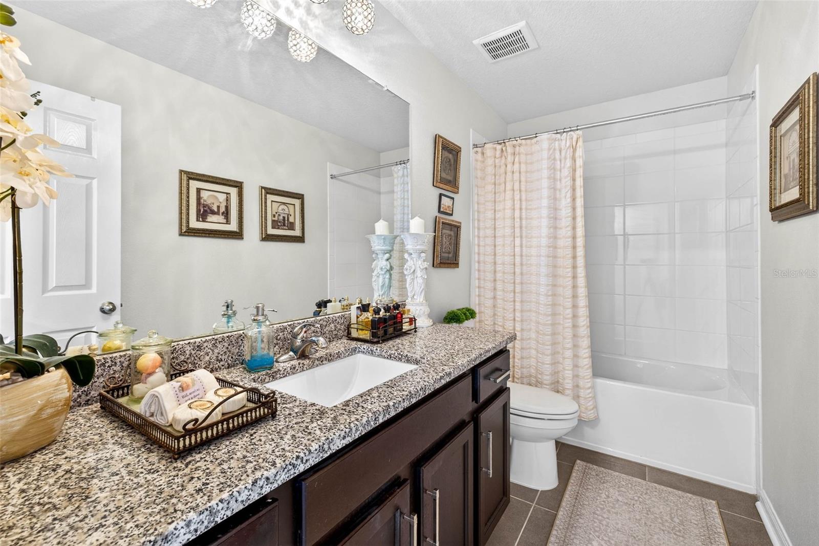 Secondary bathroom with tub/shower combination, wooden cabinetry, granite countertops and tiled flooring