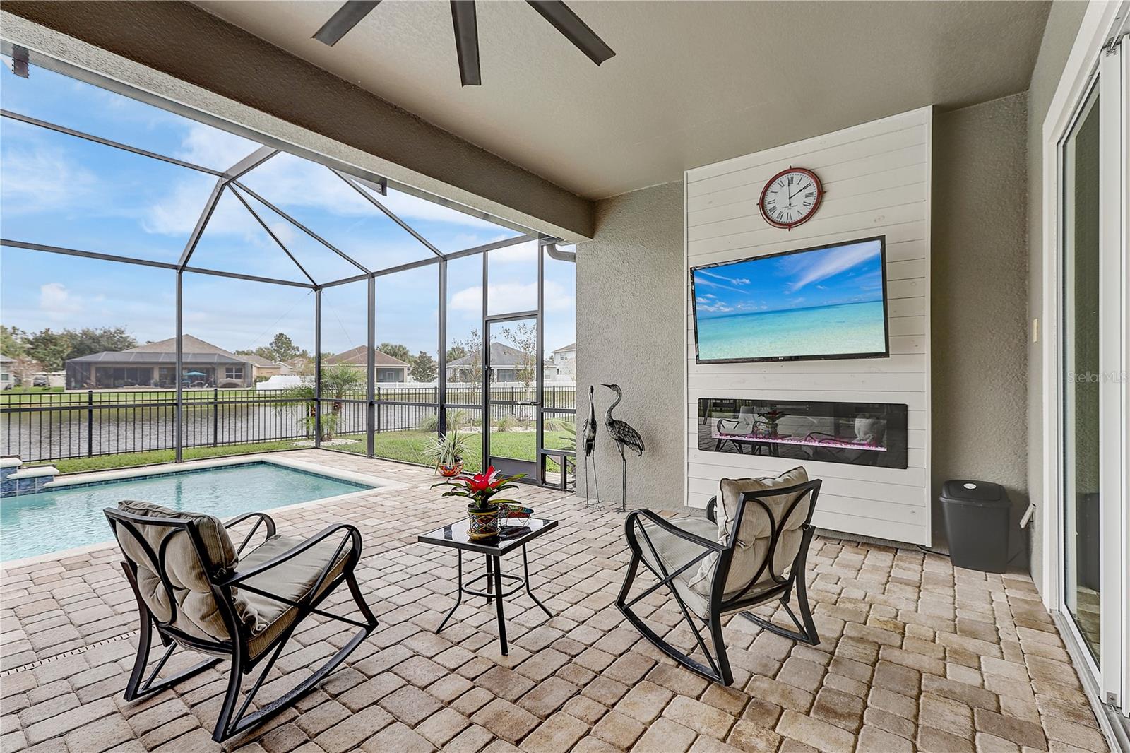 paved and partially covered screened in lanai with a gas operated fireplace and outdoor kitchen that overlooks your saltwater heated pool and pond views