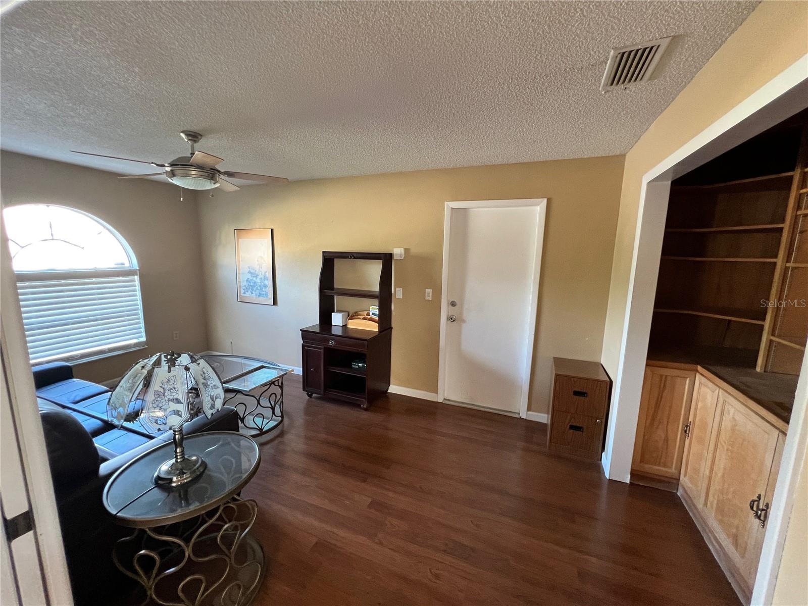 View of fourth bedroom/office/den from near front entry and living room. Single door on far wall is entry to garage. Doorway on right is closet with built-in cabinetry (and closet doors removed).
