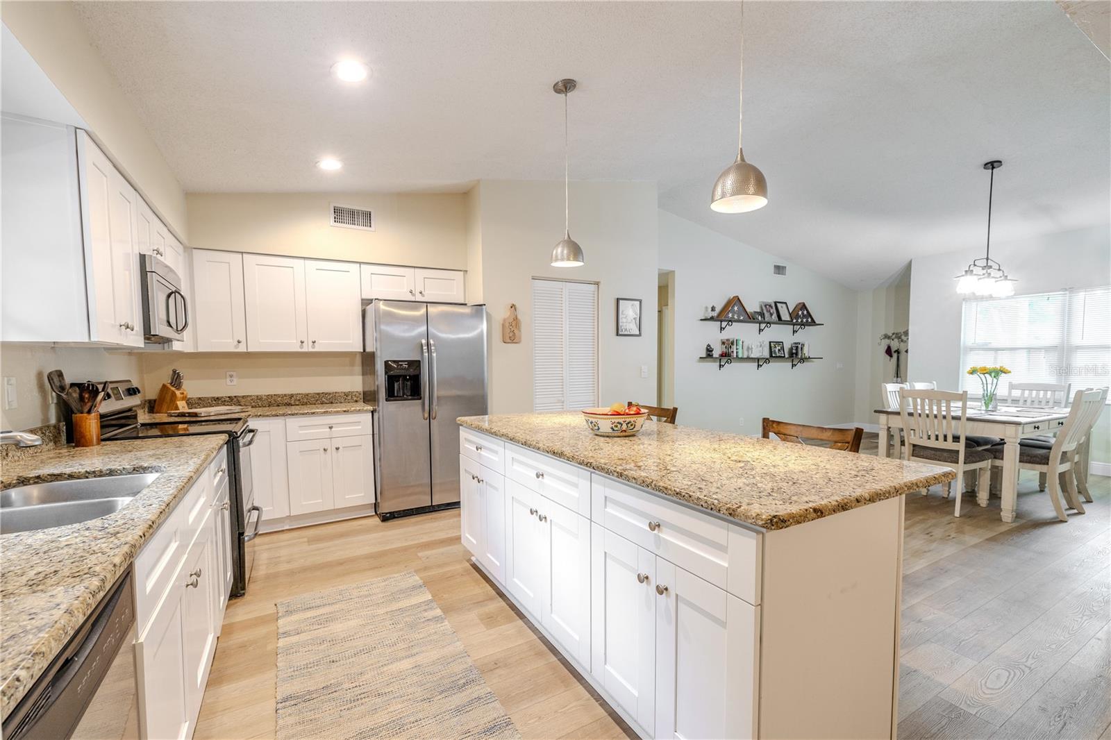 Airy open-concept kitchen and dining area featuring granite counters, white cabinetry, stainless appliances, recessed and pendant lighting, and an oversized island with abundant storage—ideal for entertaining.