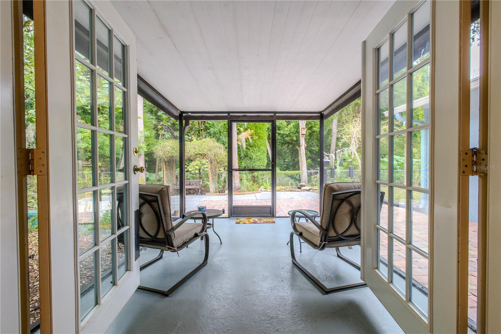Screened porch off the living room with French-door access, a covered ceiling, and peaceful views of the brick paver patio and lush backyard greenery and active preserve bird watching.