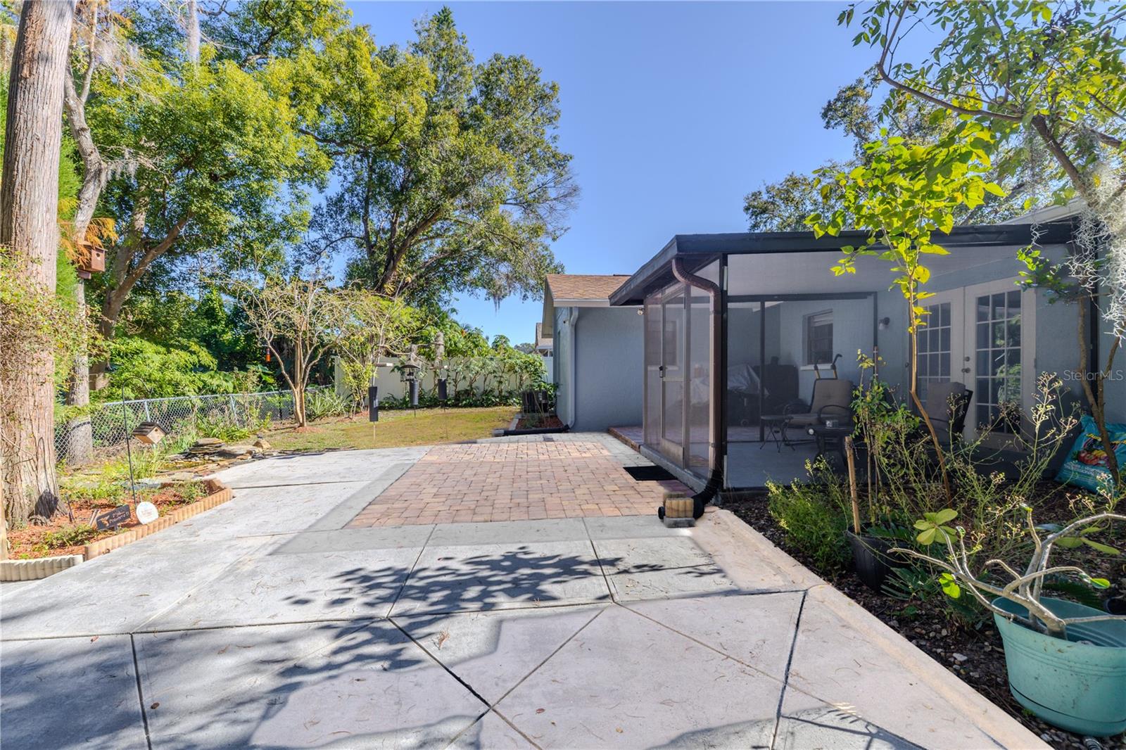 Spacious backyard entertaining area featuring an expansive patio and paver space, plus a screened porch and lush, private greenery creating a tranquil outdoor escape.