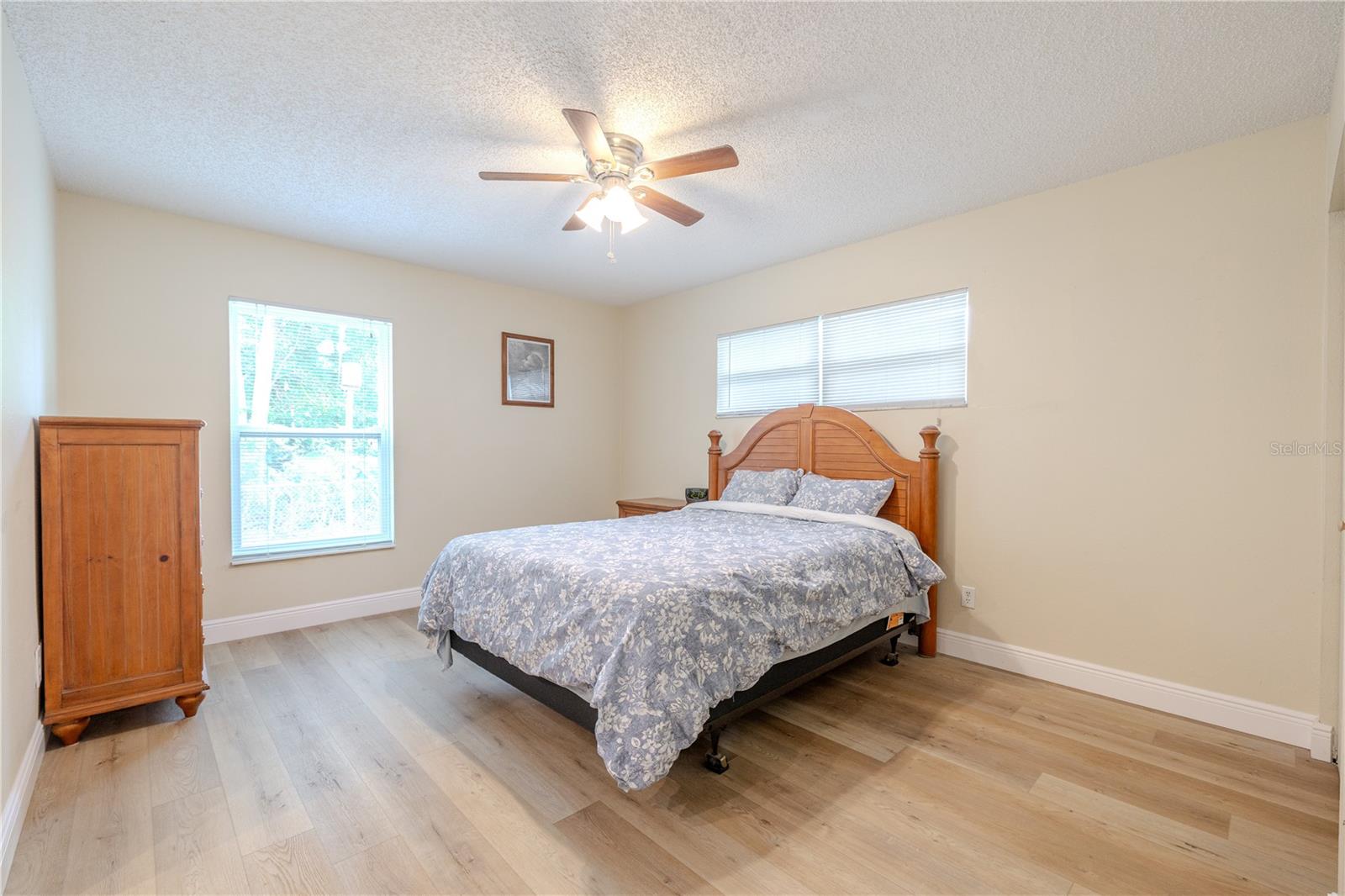 Spacious 17 X 14 ft. primary bedroom featuring wide-plank vinyl wood flooring, 5" wood baseboards, a ceiling fan, and bright natural light from multiple windows for a calm, comfortable retreat.