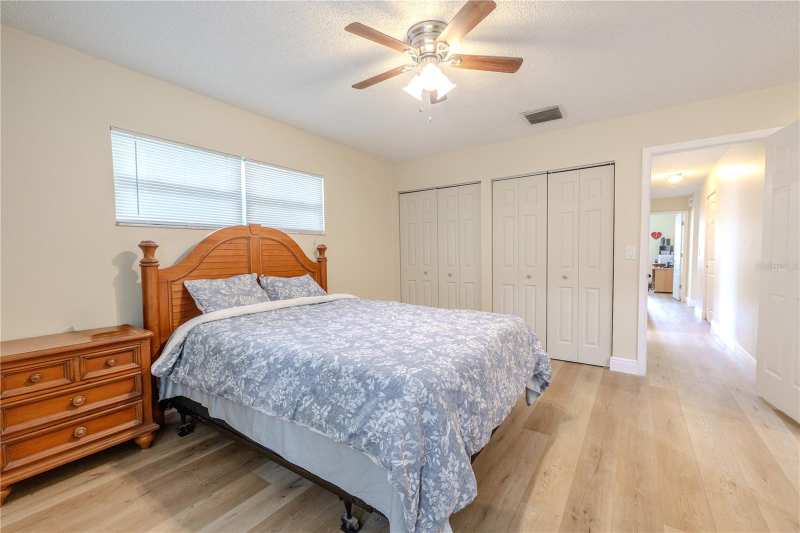 Additional view of the spacious 17 X 14 ft. primary bedroom featuring wide-plank vinyl wood flooring, 5" wood base boards, dual his and her built in closed, a ceiling fan, and bright natural light from multiple windows for a calm, comfortable retreat.