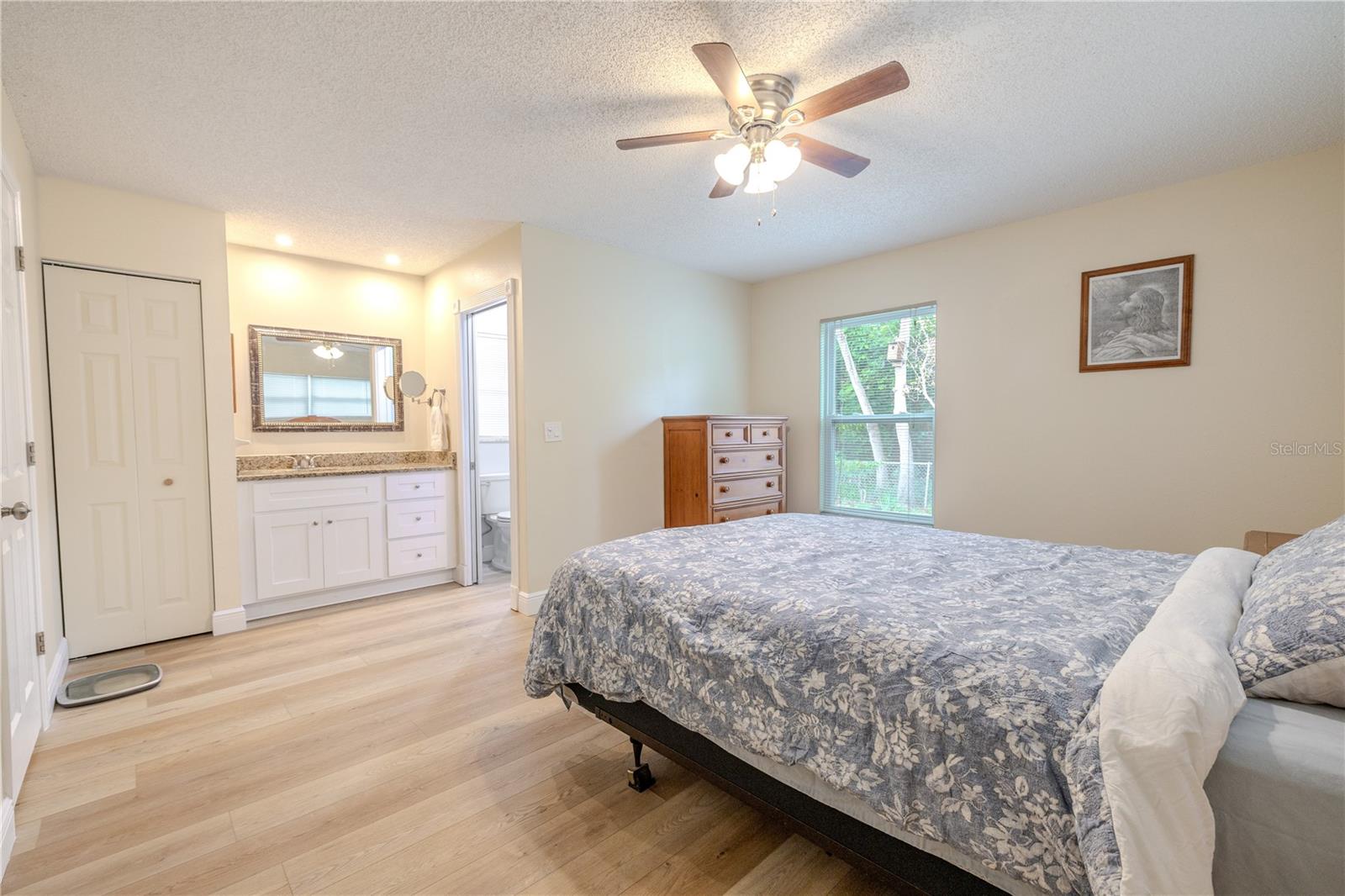 Primary bedroom suite with wide-plank vinyl wood flooring and ceiling fan, featuring a vanity area with granite counters and direct access to the private bath.