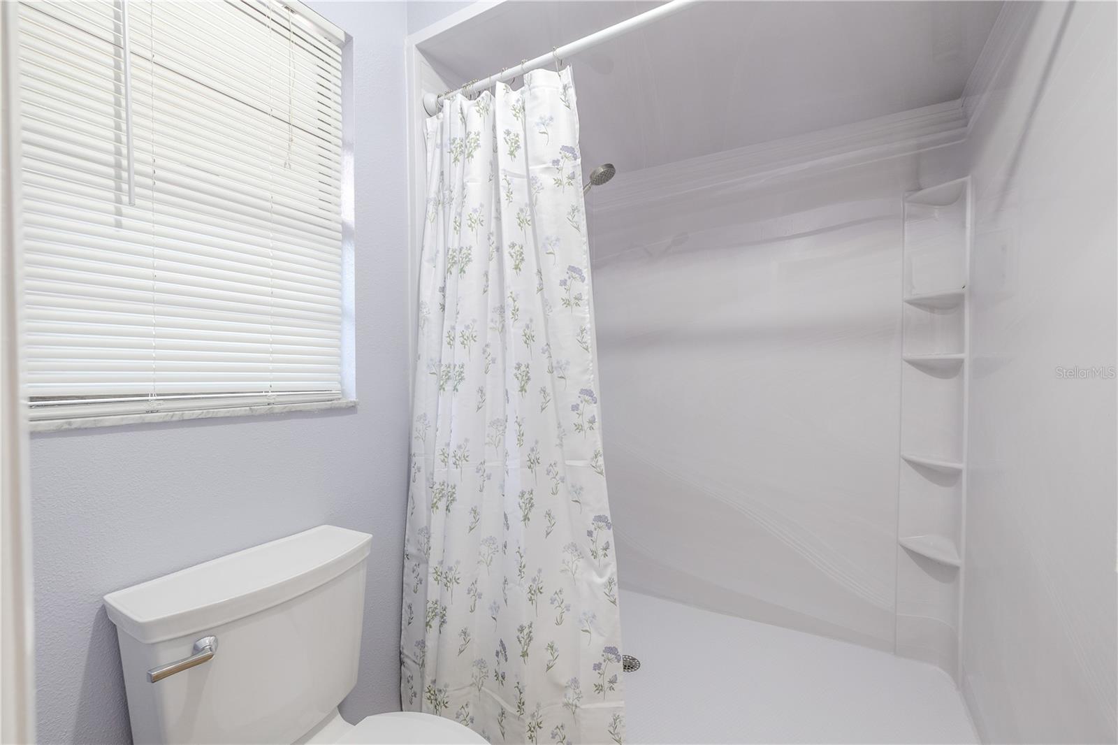 Bright primary bath with a clean extra large walk in shower, built-in shelving, and a privacy window that brings in natural light.