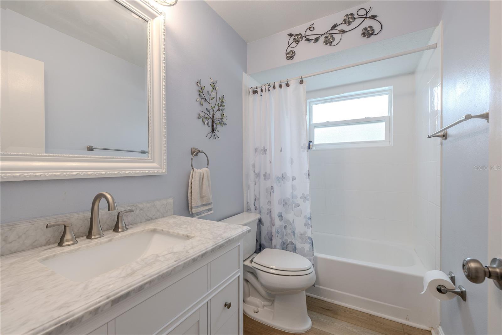 Updated full second bath featuring a marble-look vanity, modern fixtures, and a bright tub/shower combo with a privacy window for natural light.
