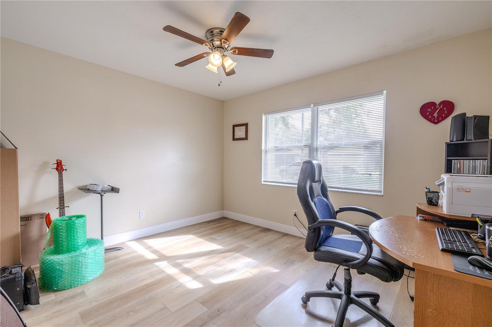 Bright second bedroom with wide-plank vinyl wood flooring, a ceiling fan, and a large window that fills the room with natural light—perfect for a guest room, office, or flex space.