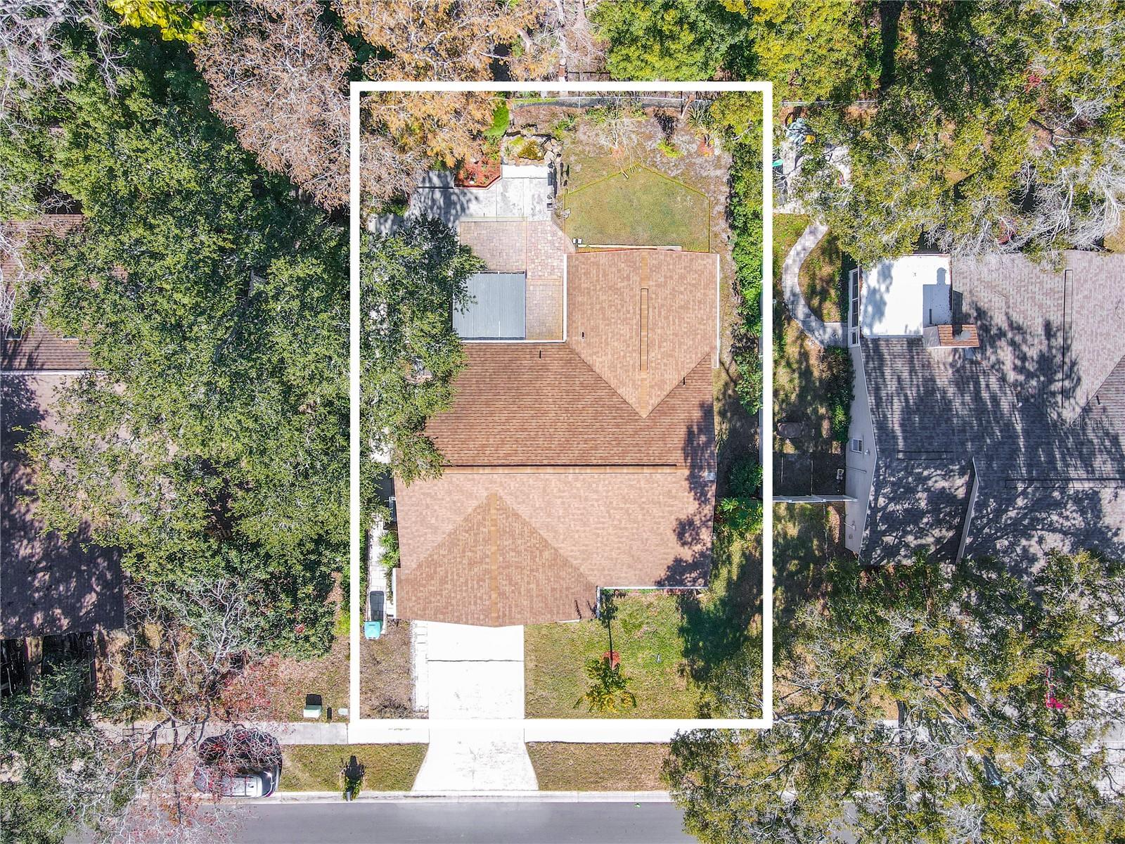 Overhead aerial view outlining the full homesite, highlighting the home’s footprint, driveway, and generous yard space surrounded by mature trees for privacy.