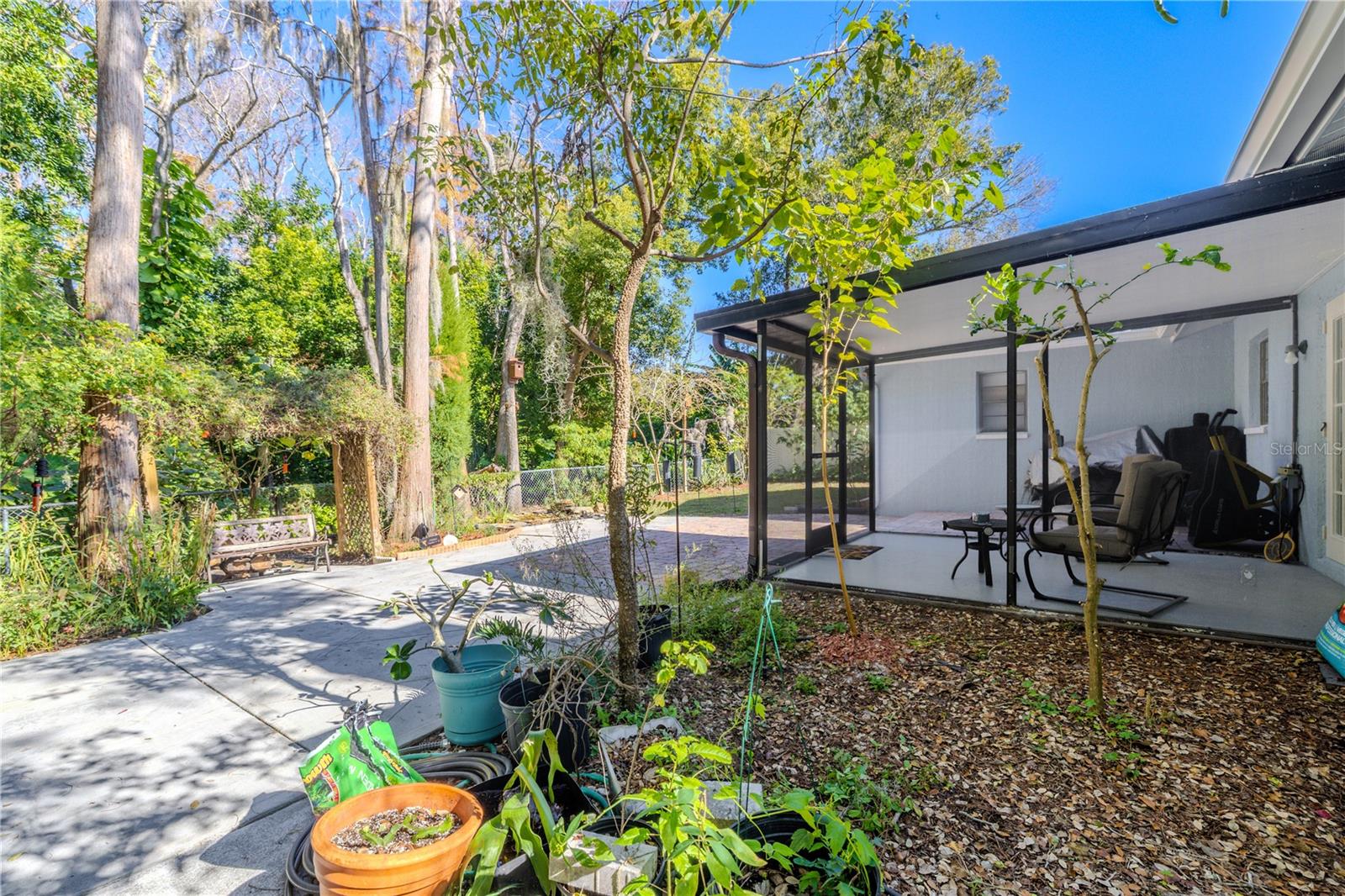 Spacious backyard area featuring an expansive patio and paver space, plus a screened porch and lush, private greenery creating a tranquil outdoor escape.