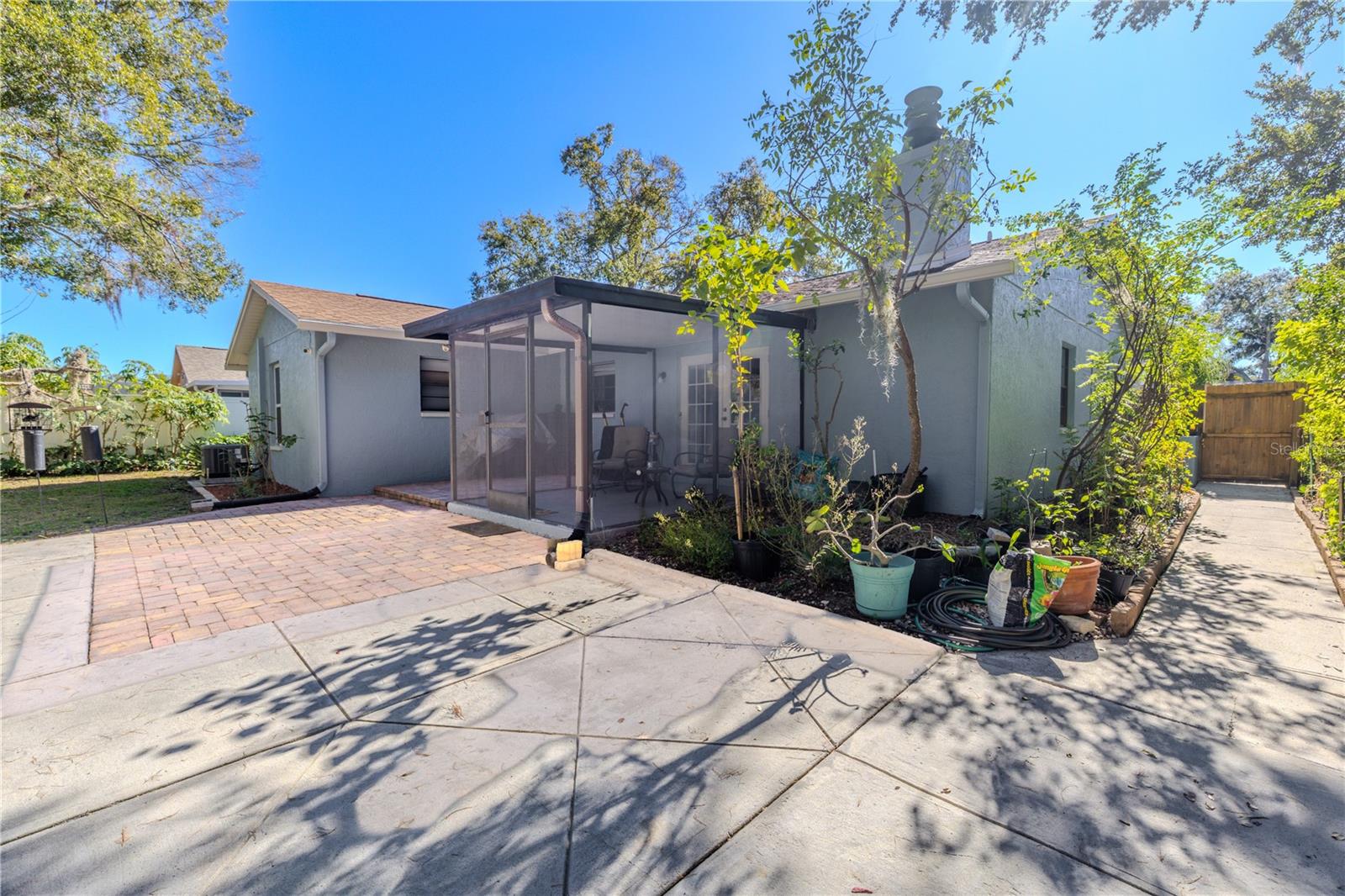 Broader view of the spacious backyard entertaining area featuring an expansive patio and paver space, plus a screened porch and lush, private greenery creating a tranquil outdoor escape with exterior gated access.