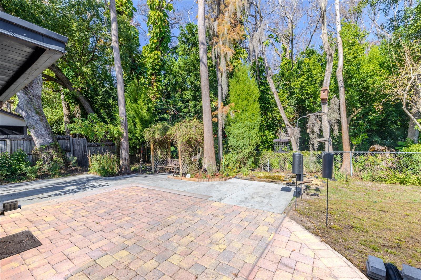 Expansive paver patio and outdoor living space surrounded by towering trees and lush preserve views, creating a private, shaded setting for relaxing or entertaining.