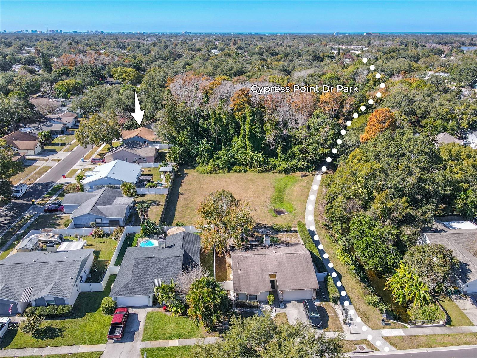 Aerial view highlighting the home’s location (arrow) directly near Cypress Point Dr Park and the surrounding greenbelt/trail corridor for easy access to outdoor recreation and nature.