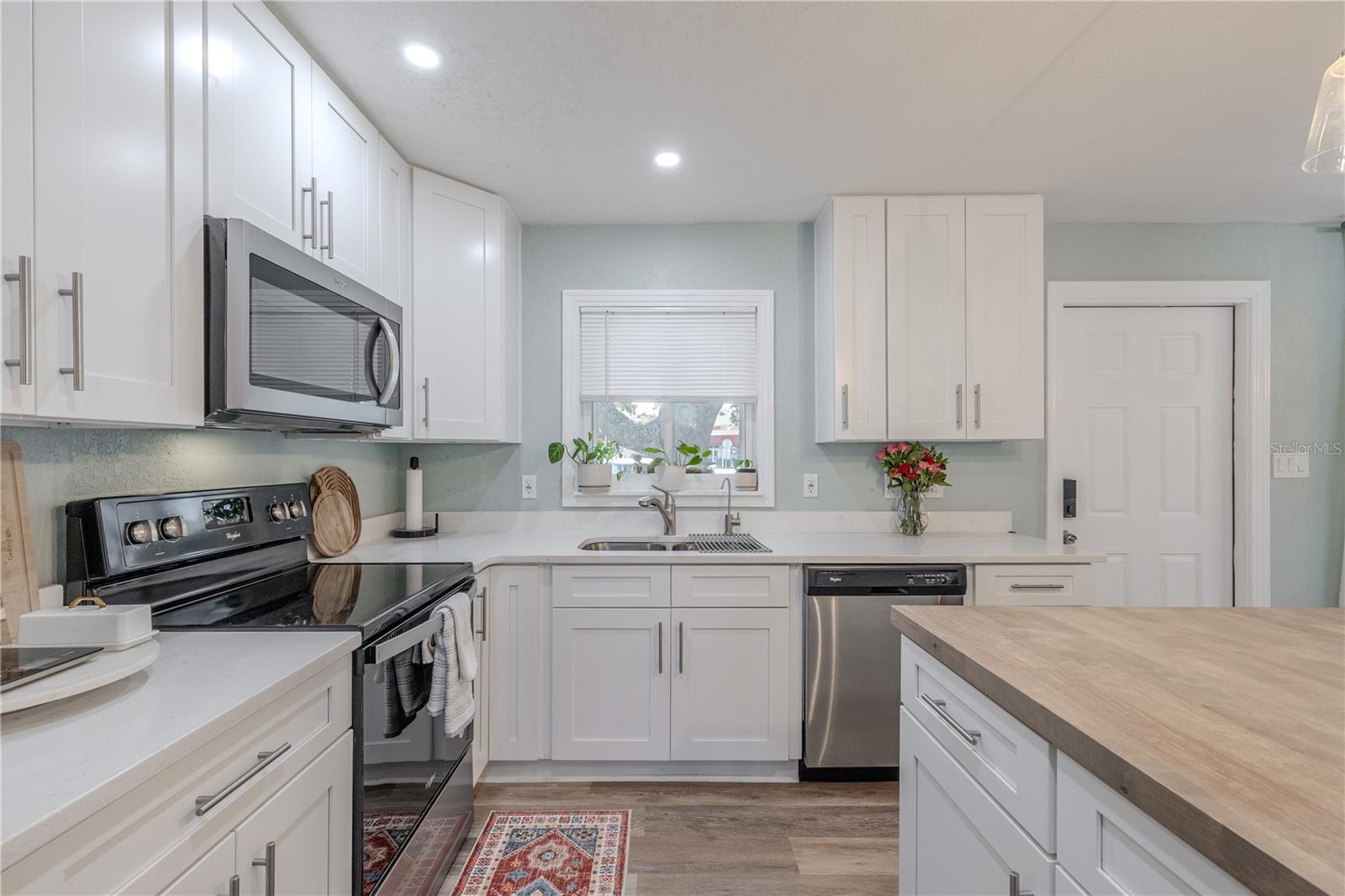 Bright kitchen features shaker cabinetry, stainless appliances, and quartz-style counters, plus a large island and a window over the sink for an airy, modern feel.