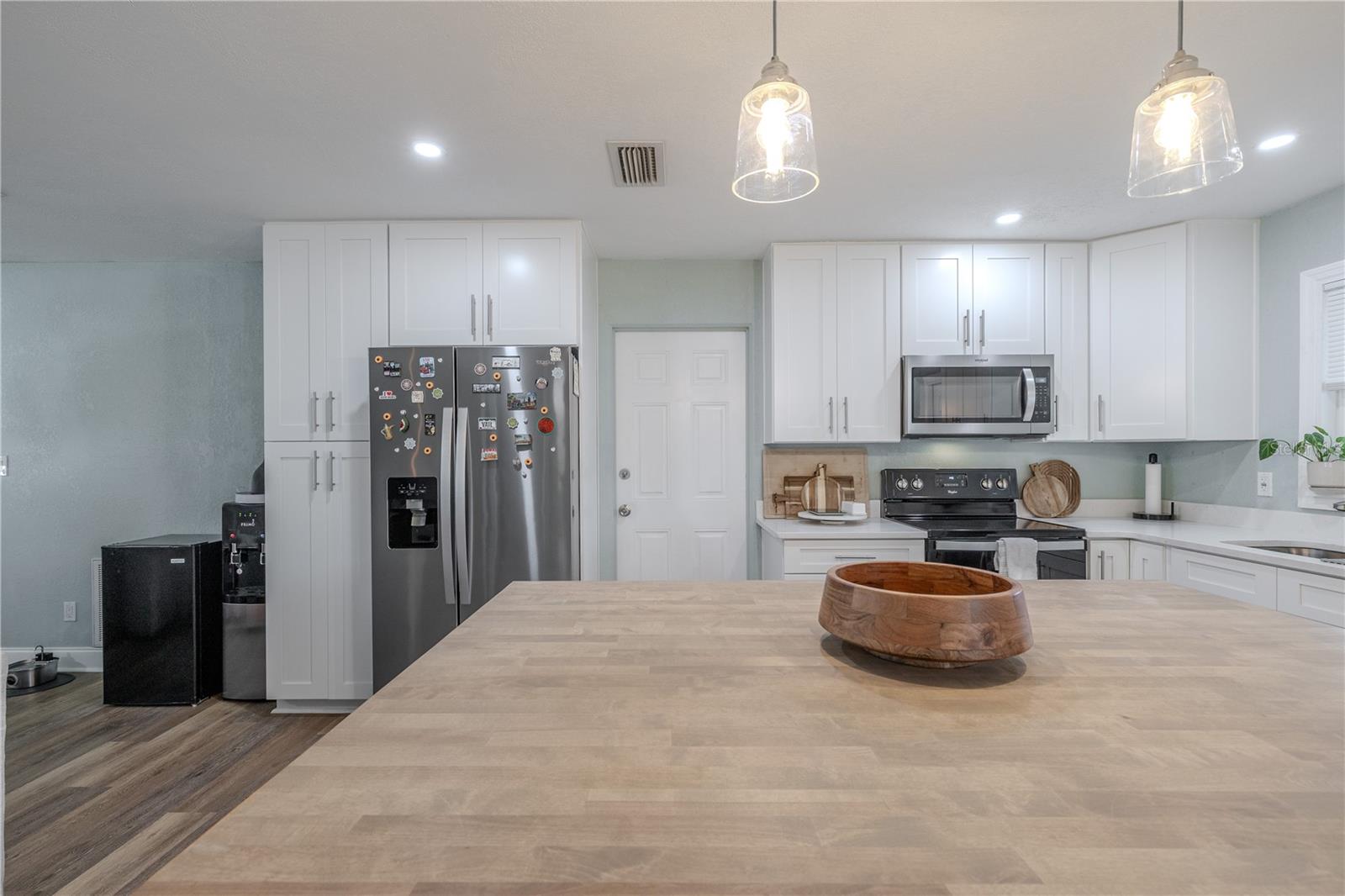 Entertain with ease in this modern kitchen featuring garage access, abundant white cabinetry, stainless appliances, and an oversized island with warm butcher-block style counters under stylish pendant lighting.