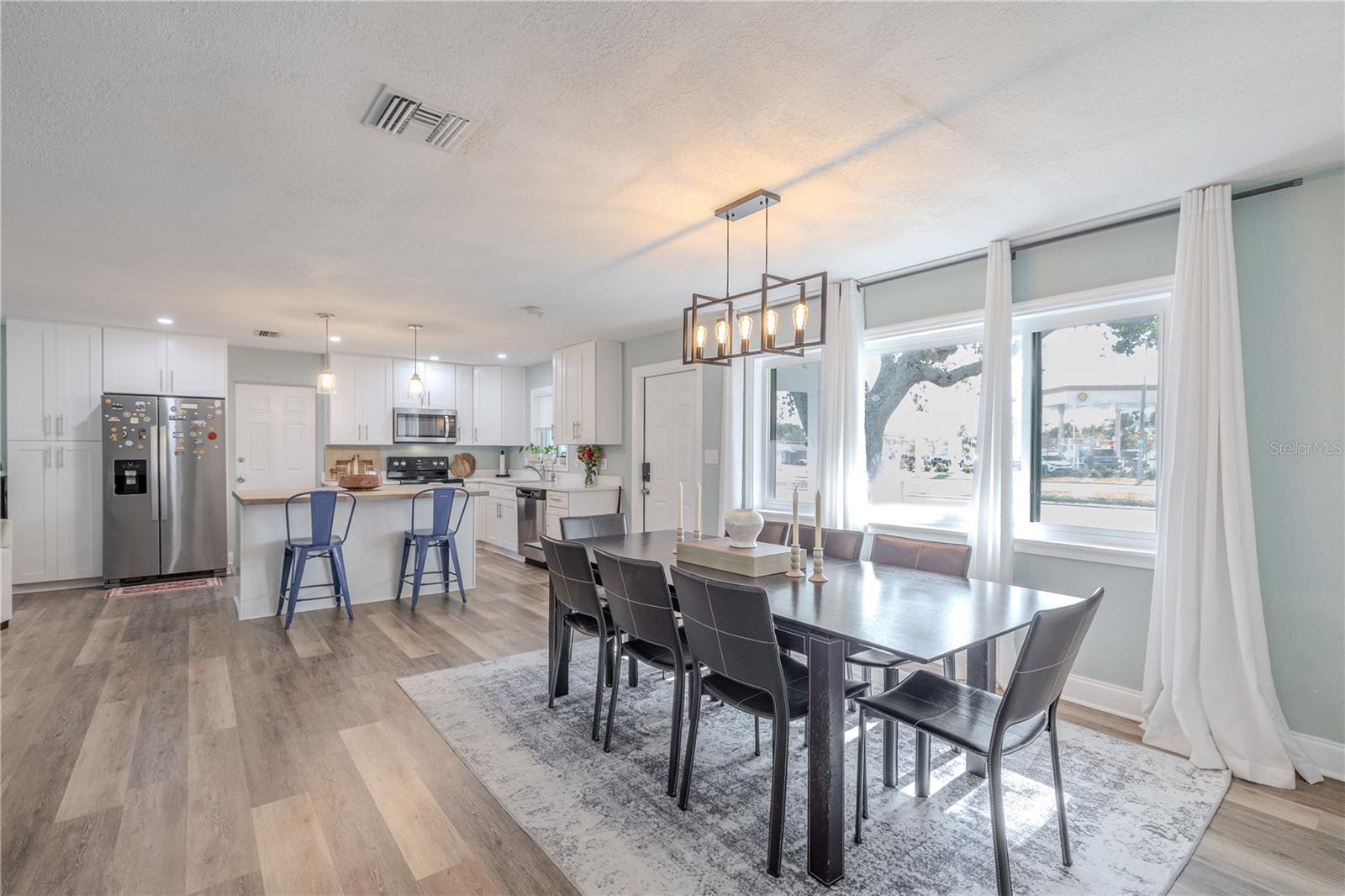 Bright open dining area features a modern chandelier, oversized windows, and seamless flow to the kitchen with a breakfast bar—ideal for everyday living and entertaining.